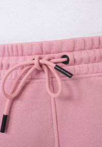 Lichtroze sweatpants hebben een elastische tailleband met een trekkoord en zwarte accenten. Het materiaal lijkt zacht met een gladde textuur.