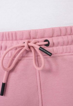 Lichtroze sweatpants hebben een elastische tailleband met een trekkoord en zwarte accenten. Het materiaal lijkt zacht met een gladde textuur.