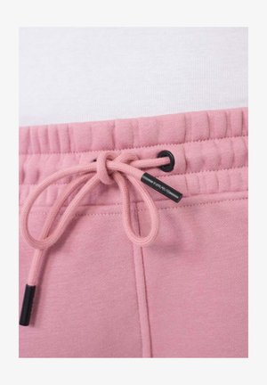 Un pantalon de survêtement rose clair avec une taille élastique et un cordon de serrage, orné d'accents noirs. Le matériau semble doux avec une texture lisse.