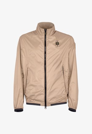 Giacca leggera beige con collo alla coreana, cerniera frontale nera, polsini ed orlo elasticizzati e una piccola patch logo nera e gialla sul petto.