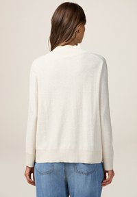 Maglione beige chiaro con una finitura testurizzata e sottili fossette. Presenta un colletto e dei polsini a coste, e una vestibilità rilassata sul retro.