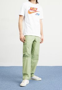 Vit bomulls-T-shirt med ett färgglatt Nike-grafiktryck. Gröna cargobyxor med sidofickor. Vita sneakers med texturerad yta.