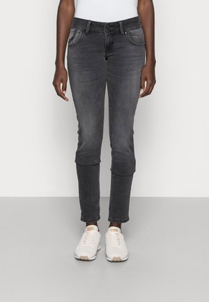 Person wearing faded black slim-fit jeans with double button closure and white sneakers, standing against a plain background.