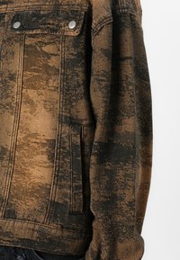 Džinsinis švarkas su tekstūruotu rudu ir juodu raštu, turintis sidabrinius akcentus, mygtukų užsegimus ir šonines kišenes.