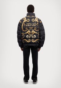 Must mustriga musta jope, millel on kuldsed barokkstiilis mustrid ja "Versace Jeans Couture" tekst seljal. Omab kõrget kaela ja elastseid varrukaid.