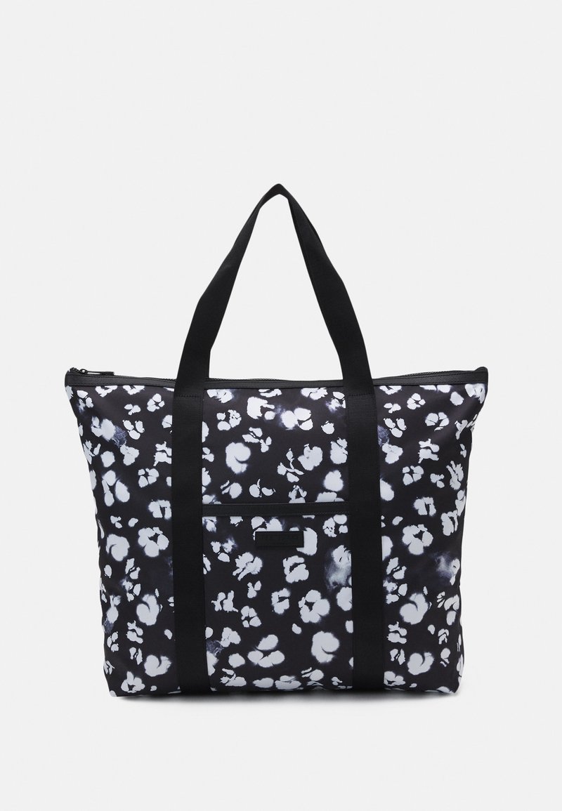 Sac cabas noir avec motif floral blanc irrégulier, deux longues anses noires, poche avant zippée et fermeture éclair sur le dessus.