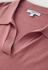 Roza polo majica z ovratnikom, mehko teksturo in etiketo z blagovno znamko „NEXT“ na izrezu za vrat.