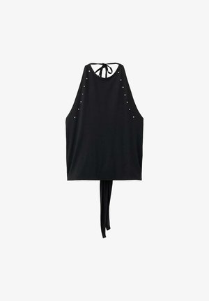 Giovane donna con capelli biondi mossi che indossa un top nero senza maniche con collo halter, borchie ai lati e vita annodata, abbinato a pantaloni bianchi.