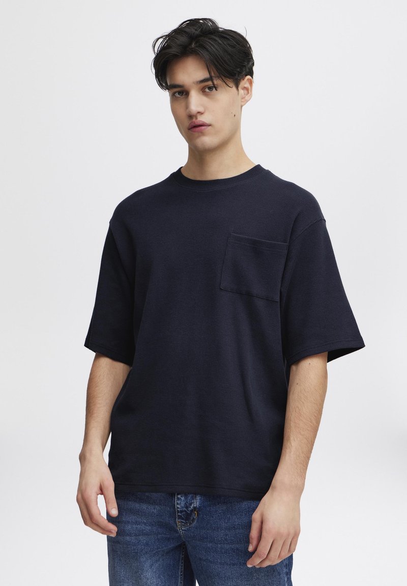 Tricou scurt cu mânecă scurtă, de culoare bleumarin, cu o croială lejeră, guler rotund și un buzunar pe partea stângă a pieptului. Fabricat dintr-un material texturat.