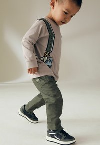 Chemise lavande à manches longues avec un design graphique de bretelles, associée à un pantalon cargo olive et des baskets grises avec des accents noirs.