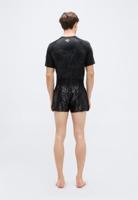 Μαύρο αθλητικό τοπ με κοντά μα νίκια και υφασματικό μοτίβο, συνδυασμένο με μαύρο σορτς με γυαλιστερό φινίρισμα και διακριτικό τύπωμα λογότυπου.