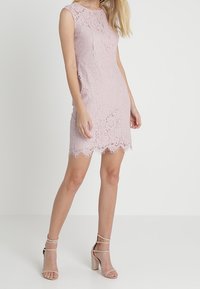 Robe en dentelle rose clair avec une coupe ajustée, sans manches, ourlet festonné, motif texturé, associée à des chaussures à talons hauts nude à brides.