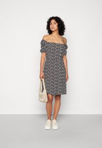 Vestido preto sem ombros com padrão floral branco, mangas curtas em balão, cintura justa, comprimento até o joelho, combinado com uma bolsa bege e ténis brancos.