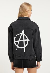 Giacca in denim nera con un simbolo di anarchia bianco stampato sulla schiena. Il design include un classico collo e dettagli con bottoni.