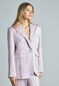 Blazer lilla chiaro con una finitura testurizzata, dotato di rever a punta, chiusura a un bottone e due tasche frontali. Tessuto liscio.