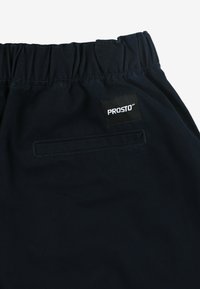 Granatowe szorty z elastycznym pasem, z tylnią kieszenią i czarną naszywką z logo PROSTO. Gładka faktura materiału, prosta forma.