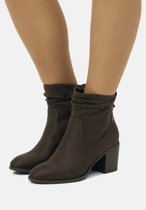 Bottines en daim marron avec un design décontracté, bout effilé et un talon bloc. Présentent des coutures discrètes et une fermeture éclair sur le côté.