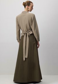 Pitkä oliivinvihreä hame, jossa on beige vyö. Kauluspaidassa on beige pitkähihaisuus, takana solmittava yksityiskohta, sileä kangas ja varsinainen istuvuus.