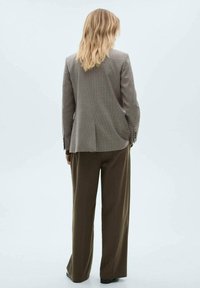 Blazer marrone a quadri con una silhouette aderente, abbinato a pantaloni marroni a gamba larga. Presenta rever classici e chiusura a due bottoni.