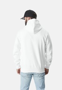 Sweatshirt blanc à capuche avec une poche kangourou et des poignets côtelés. Associé à un jean bleu clair et une casquette noire avec un bord à motifs.
