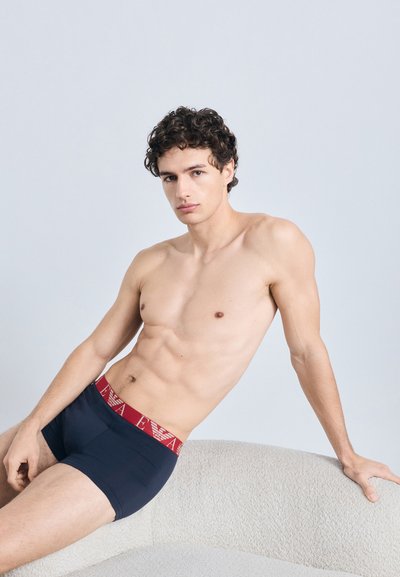 Cuecas boxer azul-marinho com uma cintura elástica vermelha que apresenta um logótipo. Tecido suave, design ajustado e corte de cintura média.