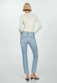 Top ajustado de manga larga en beige claro con cuello redondo y diseño de hombros sin costuras, combinado con jeans rectos de pierna azul claro.