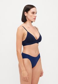 Ensemble de soutien-gorge et de bikini bleu marine en matériau lisse. Le soutien-gorge présente un décolleté en V et des fines bretelles réglables; le bikini a un design échancré.