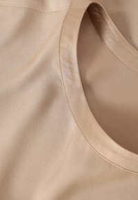 Light beige fabric with a smooth texture, featuring a rounded neckline and visible stitching, showing a close-up of the material.