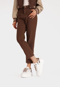 Pantaloni marroni a vita alta con una finitura testurizzata, abbinati a sneakers a piattaforma bianche con dettagli in pelle marrone e finiture metalliche.