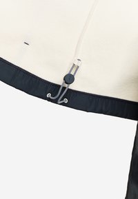 Vêtement en polaire blanche avec un ourlet élastique noir, doté d'un cordon de serrage noir et blanc et d'un bouton réglable rond.