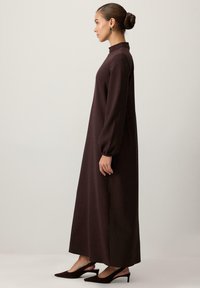 Rochie lungă, maro, cu guler înalt, mâneci tip ballon și fante laterale. Purtați cu toc înalt, ascuțit, de culoare închisă. Textură de stofă netedă.