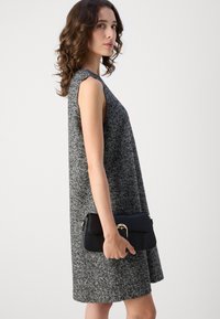 Grijze textuurloze mouwloze jurk met een losse pasvorm. Gecombineerd met een zwarte clutch met een gouden accent. Glad materiaal, eenvoudig ontwerp.