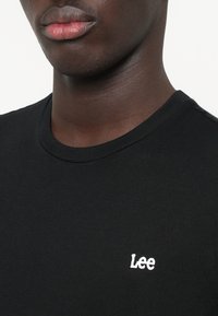 Svart bomull t-skjorte med rund hals og korte ermer. Har et hvitt brodert "Lee"-logo på brystet. Glatt tekstur.