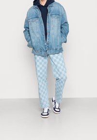 Jeansjacka med ljusblå tvätt, oversized passform. I kombination med ljusblå rutiga byxor och marinblå och vita sneakers, komplett med en huva i marinblå sweatshirt.