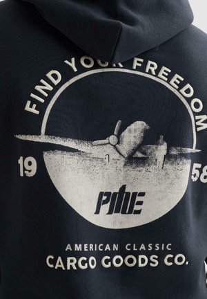 Grafik eines Vintage-Flugzeugs mit den Schriftzügen "Find Your Freedom", "1958", "Pine" und "American Classic Cargo Goods Co." auf der Rückseite eines dunklen Kapuzenpullovers.