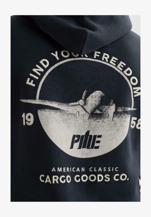 Grafik eines Vintage-Flugzeugs mit den Schriftzügen "Find Your Freedom", "1958", "Pine" und "American Classic Cargo Goods Co." auf der Rückseite eines dunklen Kapuzenpullovers.