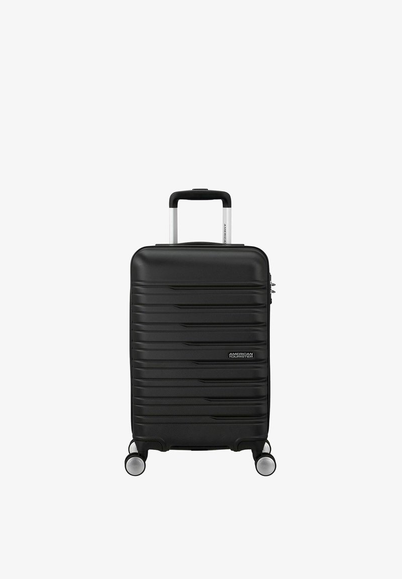 Valigia rigida nera con texture a righe, dettagli in argento, manico retrattile e quattro ruote scorrevoli. Design compatto.