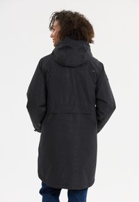 Giacca impermeabile nera con cappuccio, chiusura frontale con zip e design di lunghezza media. Tessuto morbido con una finitura liscia e accenti minimi.