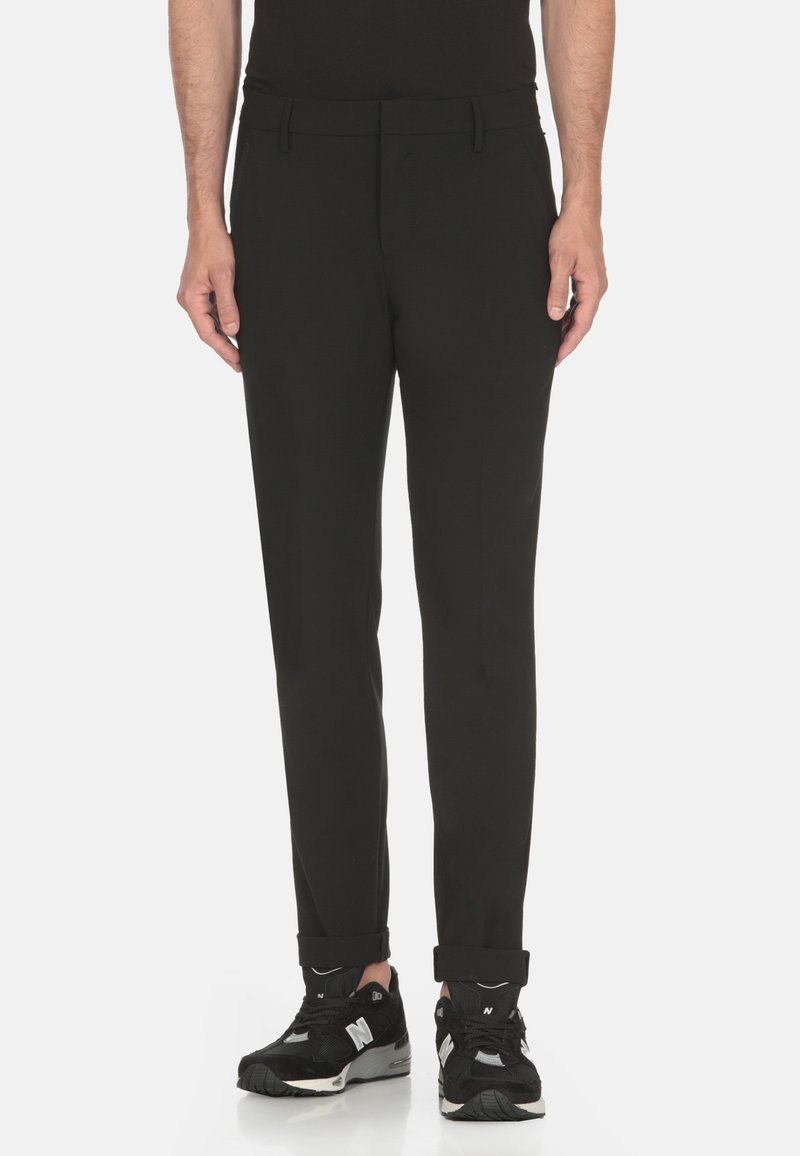 Pantaloni neri su misura con una texture liscia e una vestibilità slim, dotati di una cintura in vita e orli a polsino, abbinati a scarpe da ginnastica nere.