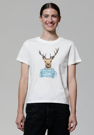 T-shirt en coton blanc avec un graphique d'un cerf aux bois, portant une chemise rayée bleu et blanc. Manches courtes et col rond.