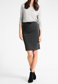 Gray long-sleeve top with a slight shimmer, paired with a black pencil skirt featuring a drawstring waist. Black ankle boots complete the look.