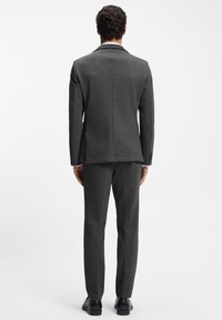 Dark gray tailored suit with textured fabric, featuring a single vent on the jacket and straight-cut trousers. Shoes are polished and dark.