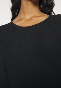 Pull noir en maille avec un large col rond, un tissage texturé et des manches longues, mettant en avant une apparence douce et confortable.