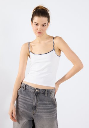 Top blanco sin mangas con ribetes a cuadros en los tirantes, diseño ajustado y textura suave. Combinado con jeans grises de cintura alta. Estilo simple y casual.