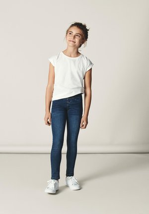 T-shirt bianco a maniche corte, jeans skinny blu e sneakers bianche. Design semplice, tessuto morbido e forma aderente senza motivi o decorazioni.