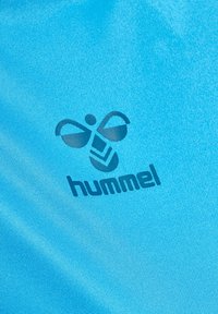 Et lyseblåt stof med et mørkeblåt logo, der har en stiliseret bi og teksten "hummel" skrevet med fed skrift. Teksturen er glat og let reflekterende.