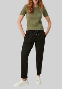 Olivengrøn kortærmet t-shirt i kombination med sorte sweatpants med snoretræk. Modellen bærer hvide sneakers. Enkel design og almindelig pasform.