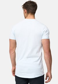 Tricou bleumarin deschis cu mânecă scurtă, guler rotund și o jumătate din spate puțin mai lungă. Material moale, neted, cu o textură simplă.