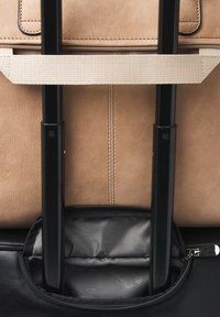 Bruine leren tas met een gladde textuur, voorzien van een ritsluiting en een ingebouwd vak voor uitschuifbare zwarte koffersleuven.
