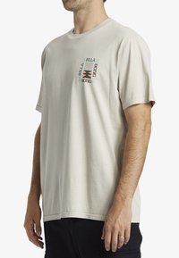 Camiseta de algodón color crema con mangas cortas, que presenta un diseño gráfico colorido en el lado izquierdo del pecho y un corte relajado.